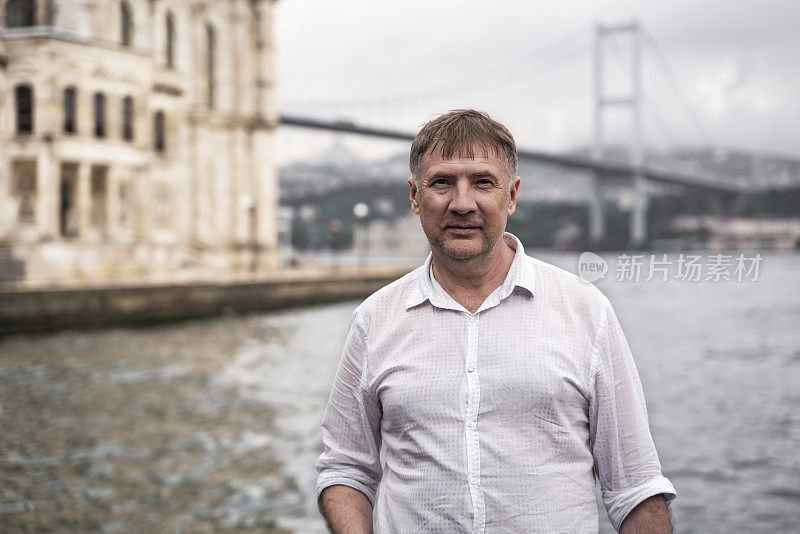 下雨天，50 ~ 55岁的男子看着镜头。背景是横跨博斯普鲁斯海峡的大桥和奥塔科伊清真寺。选择焦点，保留复制空间。